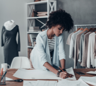 Micro-entrepreneur travaillant sur des croquis dans son atelier de travail près de vêtements accrochés aux racks
