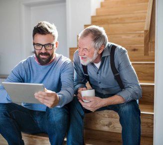 Un fils montre à son père, en utilisant une tablette, comment éviter les arnaques en ligne et sécuriser ses données. 