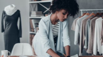 Micro-entrepreneur travaillant sur des croquis dans son atelier de travail près de vêtements accrochés aux racks